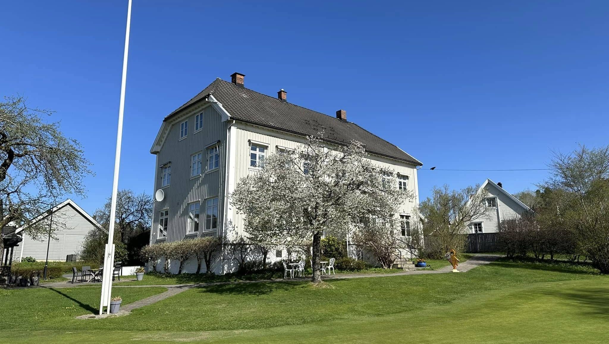 Hvit sveitservilla i hageomgivelser med blomstrende trær og putting green foran huset.